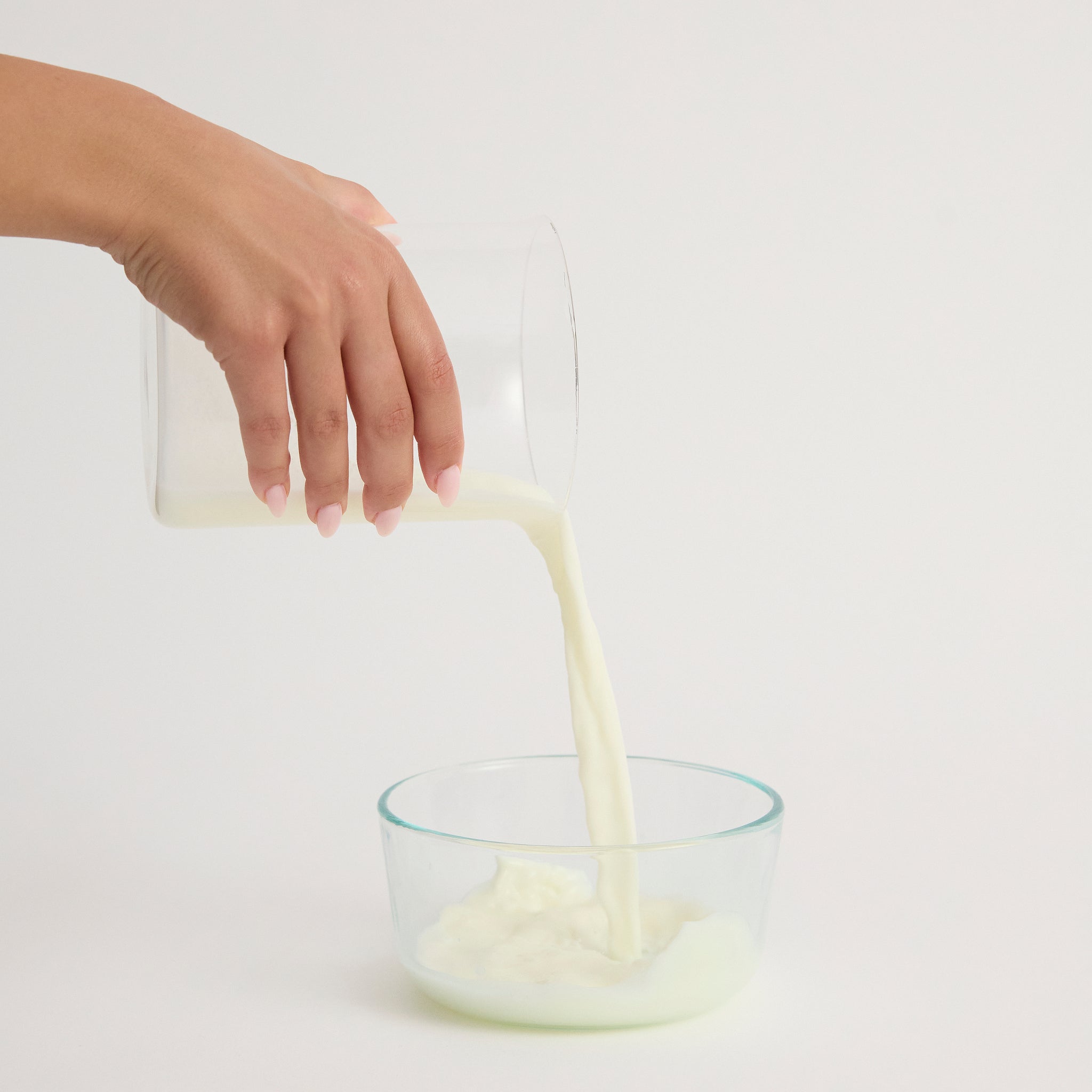 Hand pouring Di-Vetelact Nutritional Milk from a glass container into another glass bowl on a light background