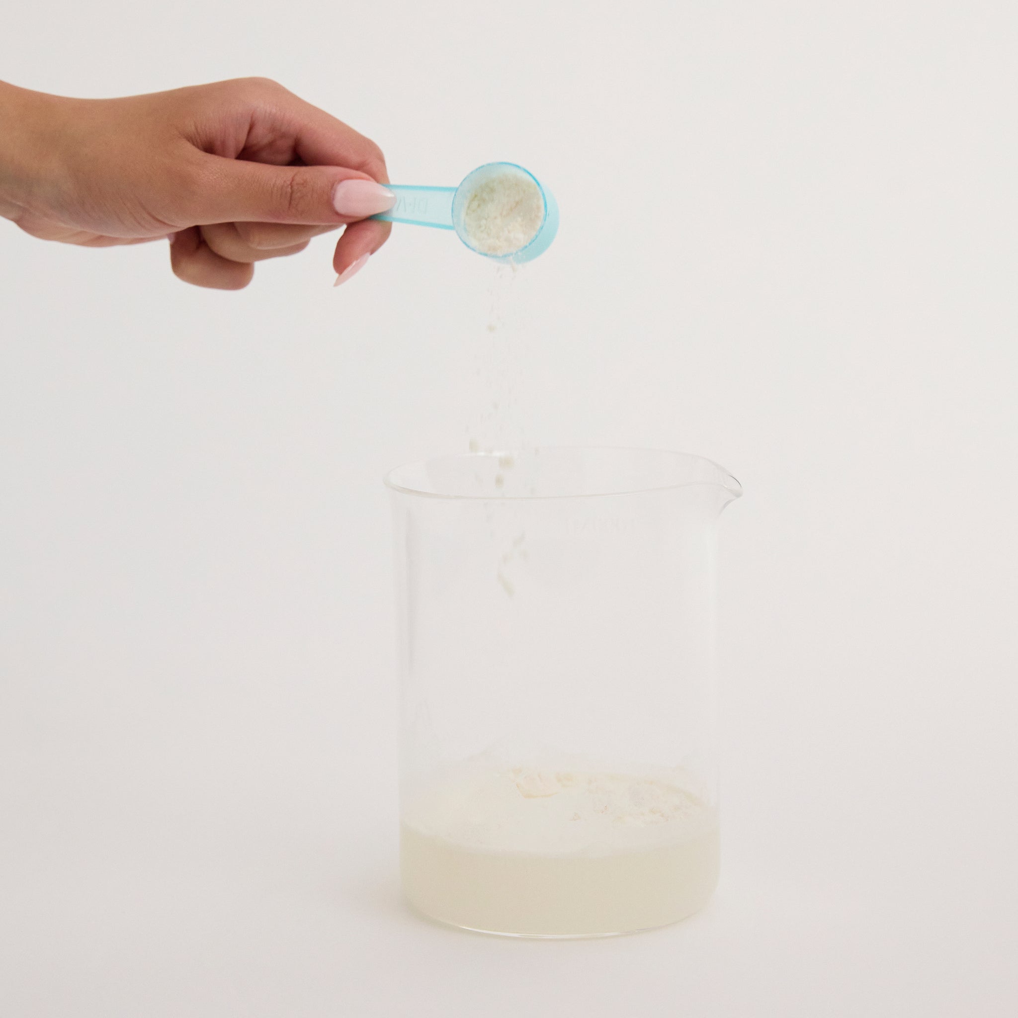 Hand tipping Di-Vetelact Scoop of Powder into Glass of water
