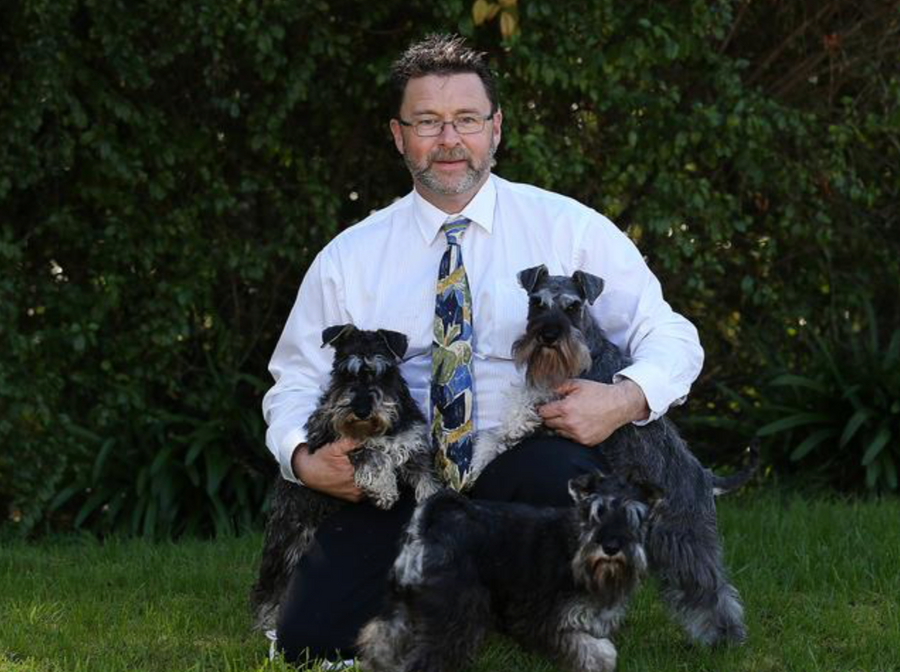 Man holding three dogs outdoors with a green background